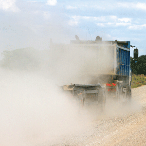 Dump truck trailing dust on a gravel road that needs Surfa-Zyme