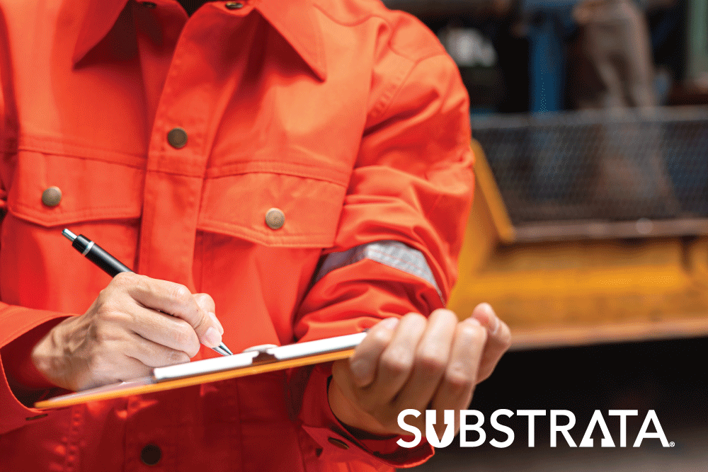 Construction worker with a clipboard standing in front of a heavy machine