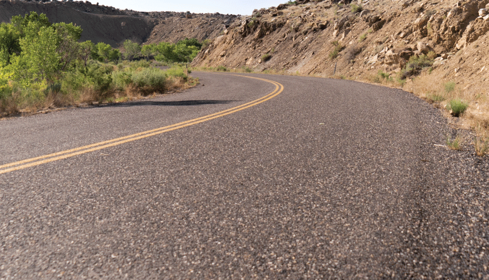 Two-lane Perma-Zyme treated paved road curving alongside a butte